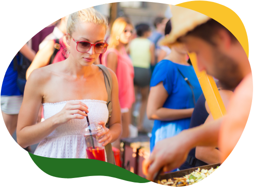 Blonda sieviete baltā vasaras krekliņā un saulesbrillēs stāv pie ēdiena stenda
